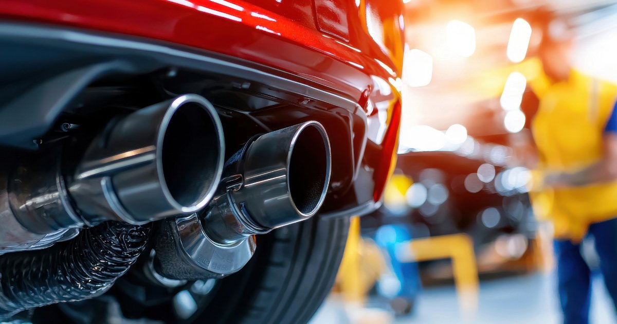 Detailed View of a Car Exhaust System Being Fixed in a Light-Filled Garage While Mechanics Work on Vehicles for Upkeep and Auto Upgrades.